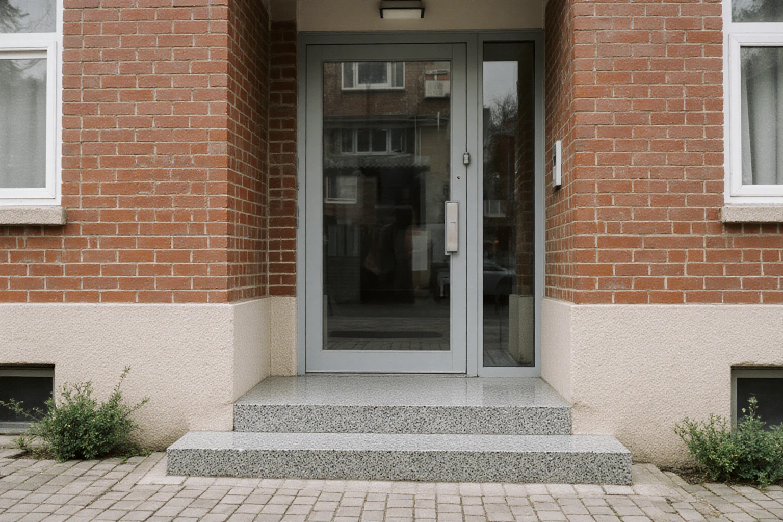 Shared glazed entrance and short staircase at a brick apartment building